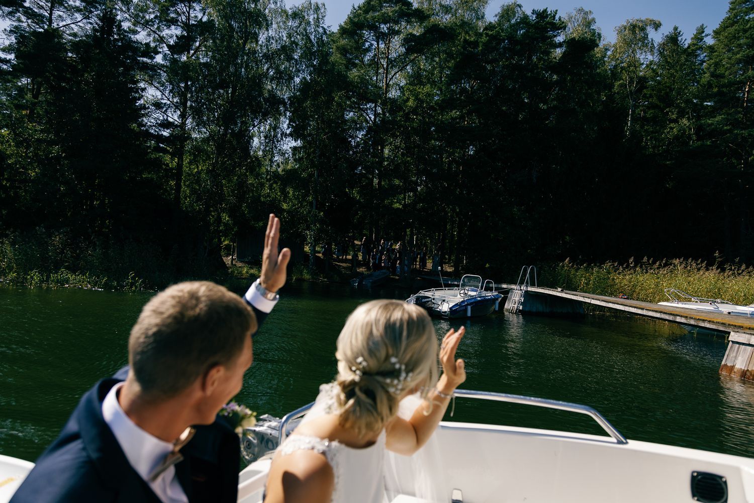 A couple enjoying a boat ride on a lake surrounded by trees on a sunny summer day.