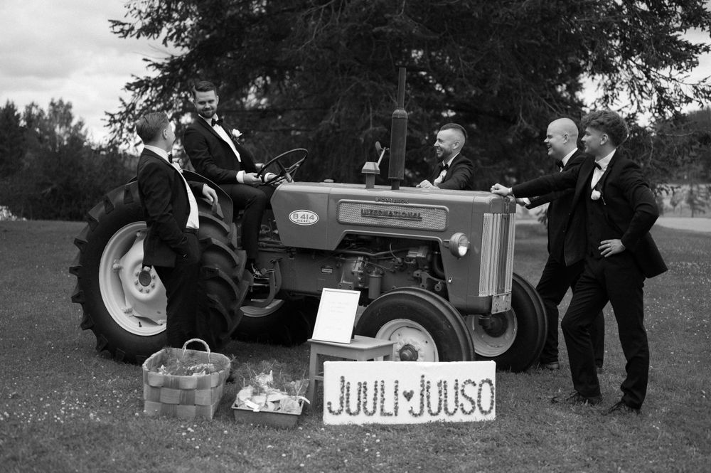 Black and white photo of wedding party members posing with vintage tractor outdoors.