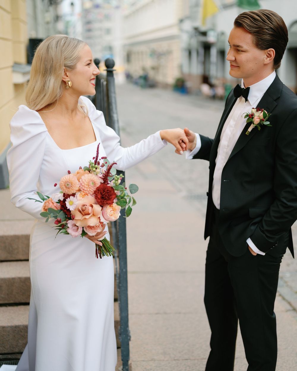 A joyful wedding moment captured on a city street with peach roses in the bouquet.