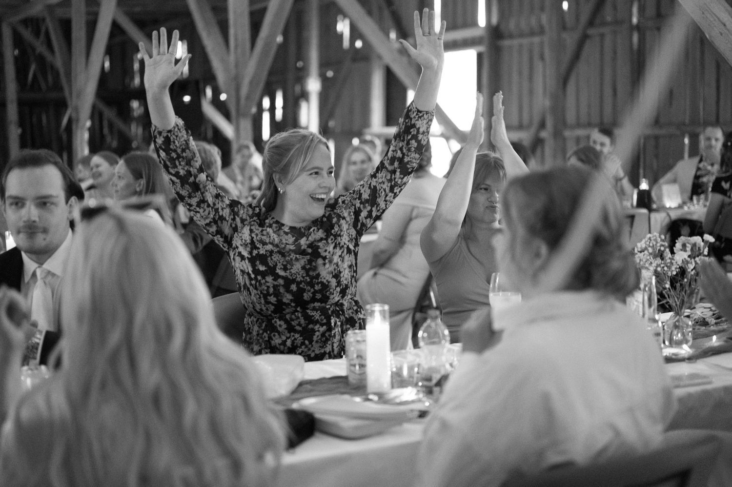 Wedding guests raise their hands in celebration during reception festivities in rustic barn.