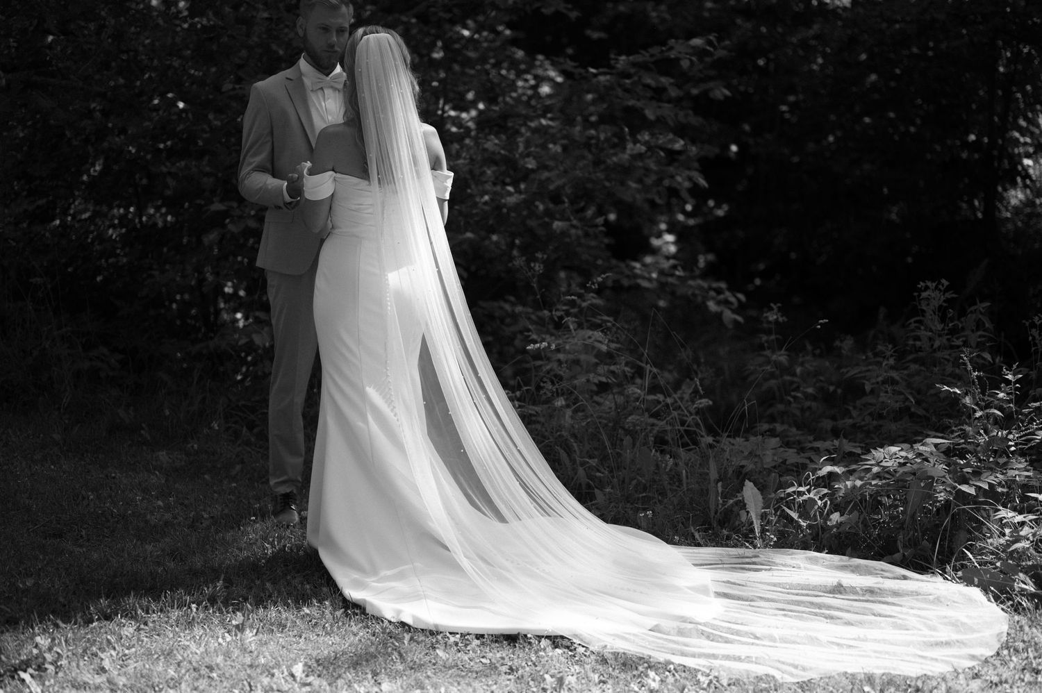 A dramatic black and white photo shows a flowing bridal train against a dark forest background.