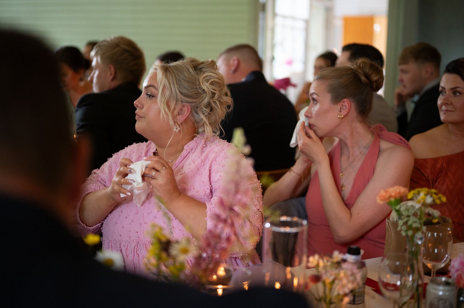 Wedding reception guests in pink attire enjoying dinner and conversation at decorated tables.