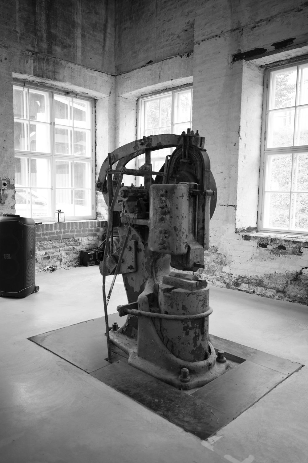 Black and white photo of vintage industrial machinery in an empty room with large windows.