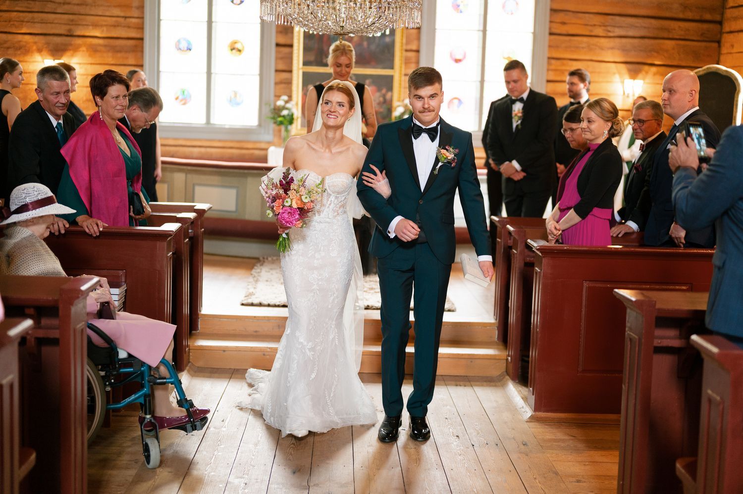 Wedding ceremony takes place in a rustic wooden chapel with guests seated in wooden pews.