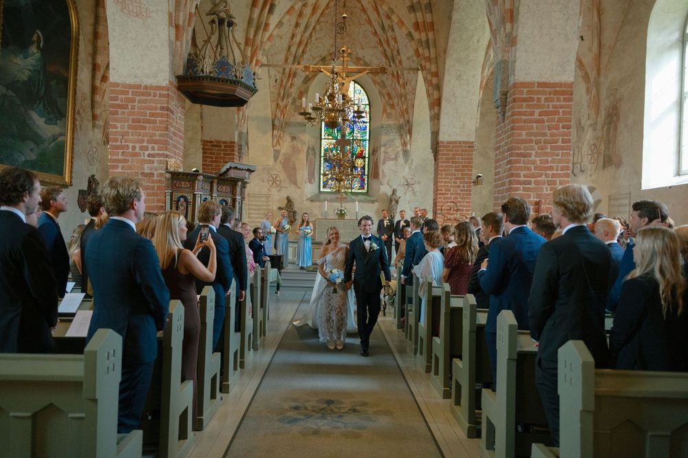 Interior view of a historic brick church with wooden pews filled with wedding guests.