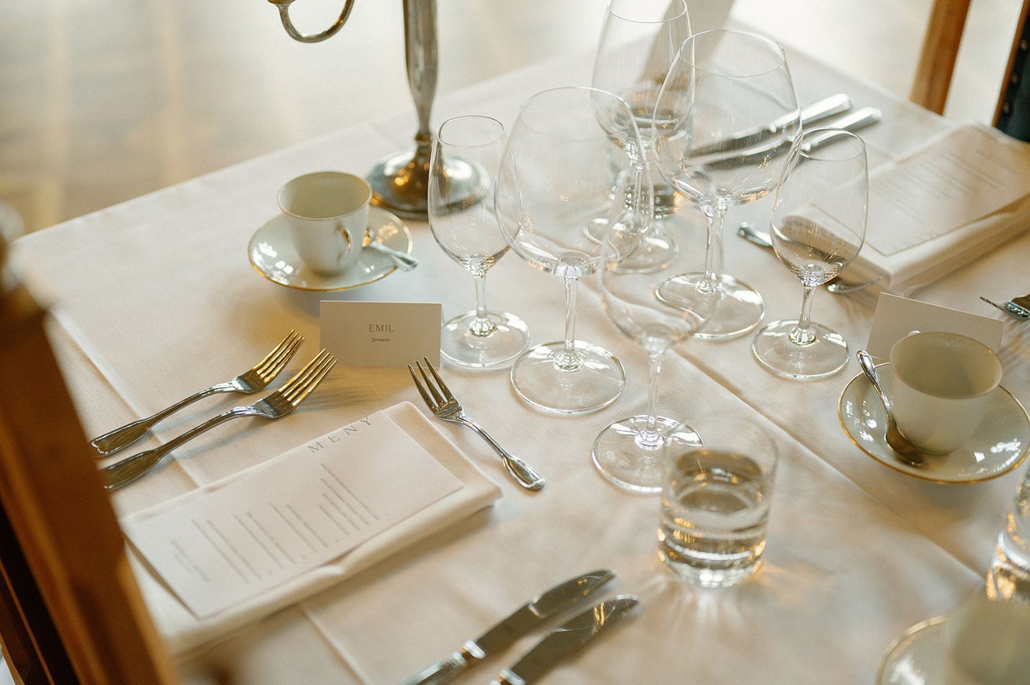 Elegant table settings with crystal glasses and white linens in natural lighting.