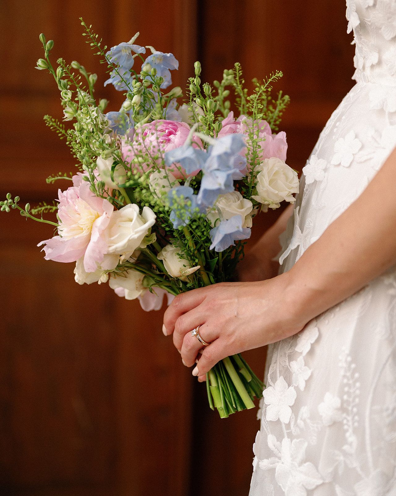 A delicate bridal bouquet with blue and pink flowers held against a white wedding dress.