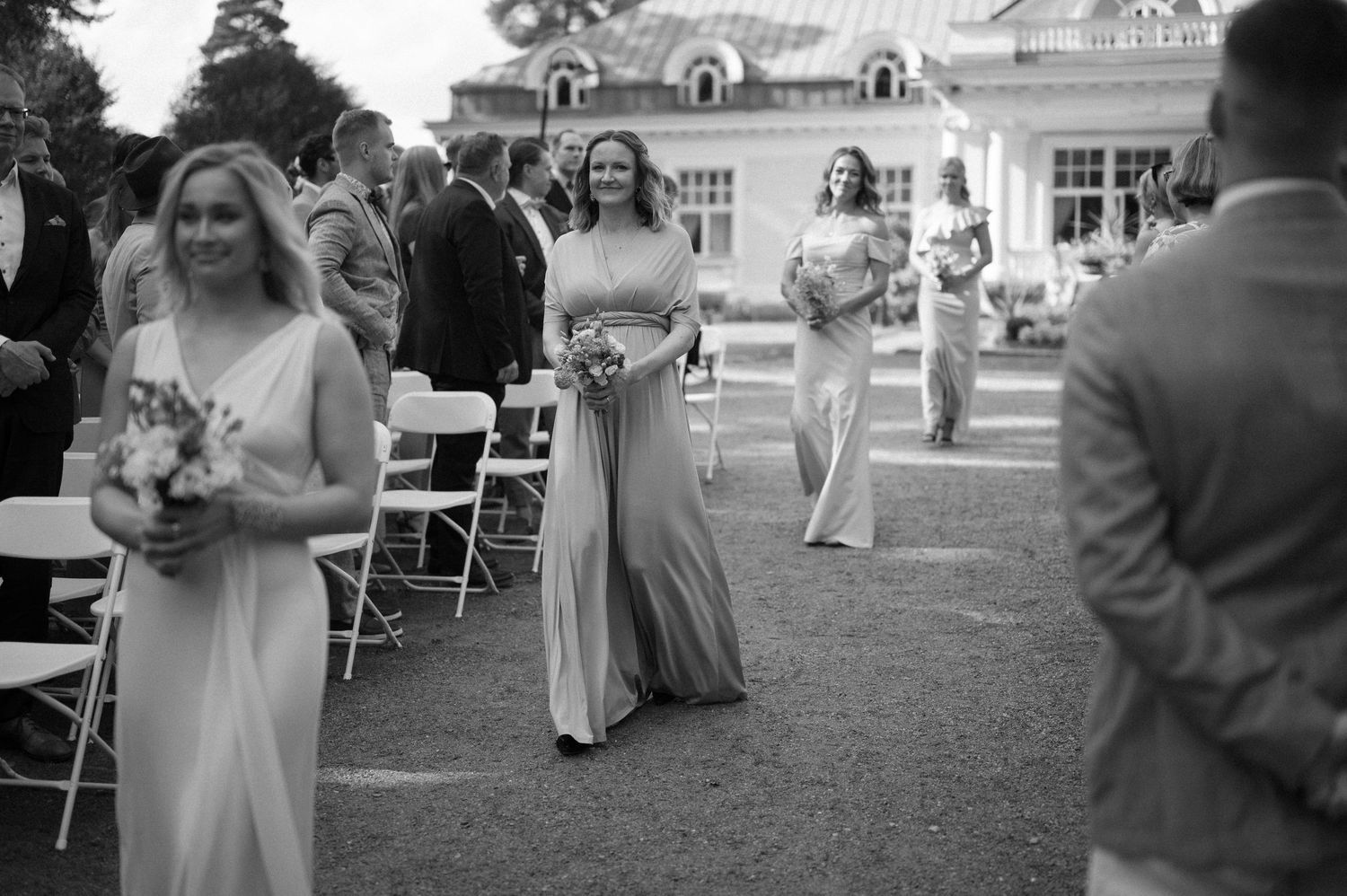 Wedding ceremony guests gather on lawn in front of stately mansion.