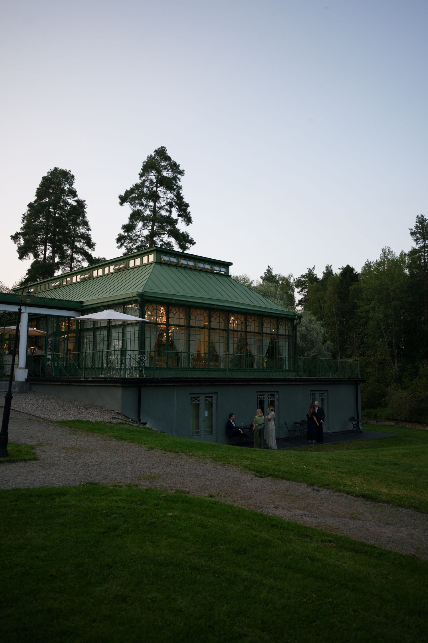 Exterior view of a modern glass and green-roofed wedding venue at dusk.