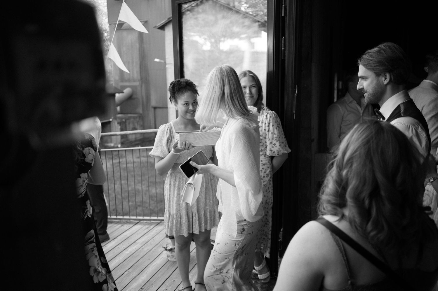 Wedding guests gather on a covered deck during a celebration, captured in black and white.