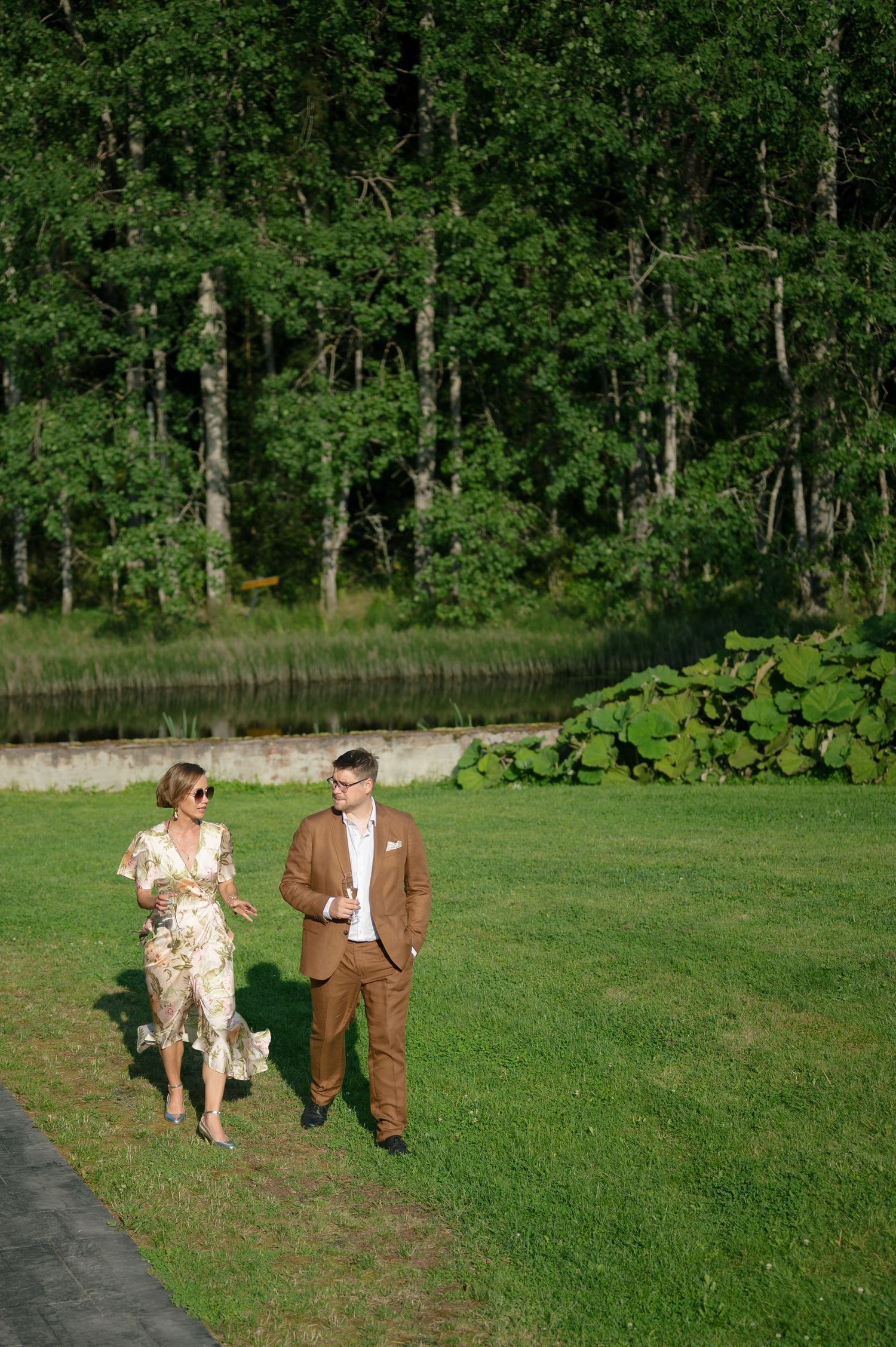 Couple walking together on grass path near wooded area.