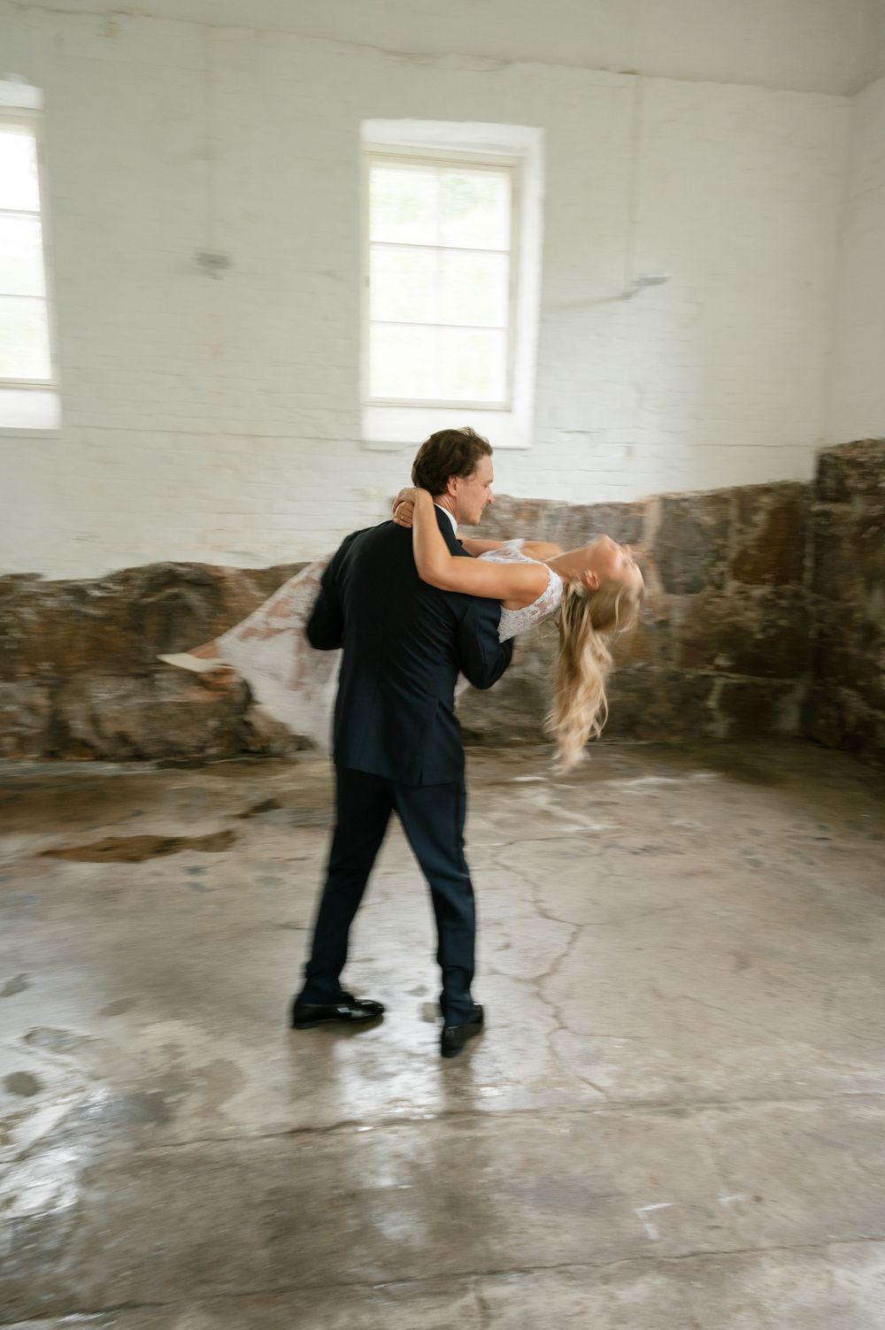 Dramatic dance dip performed in a minimalist industrial space with window light.