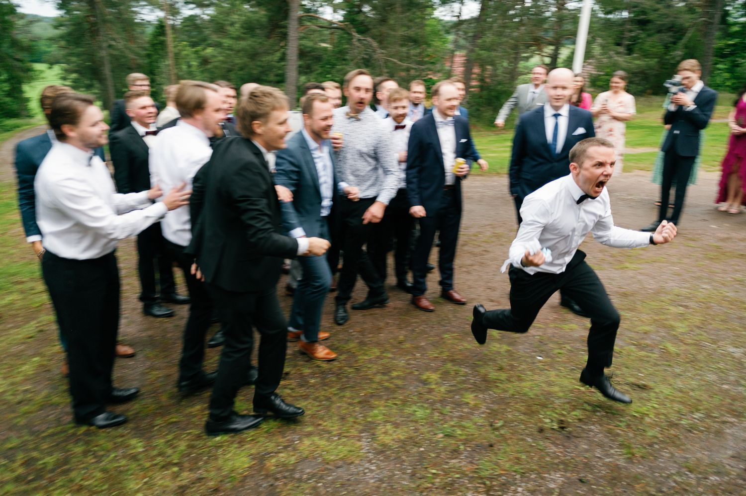 Wedding party and guests gathered on a wooded path for outdoor celebrations.