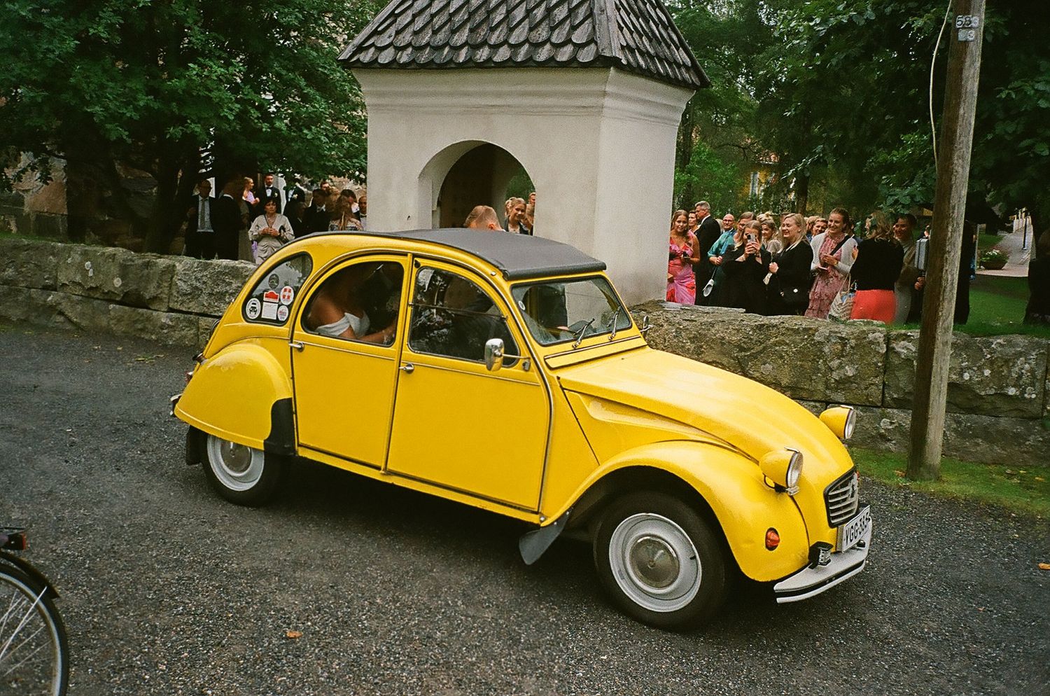 Classic yellow Citroen 2CV car parked on gravel road.