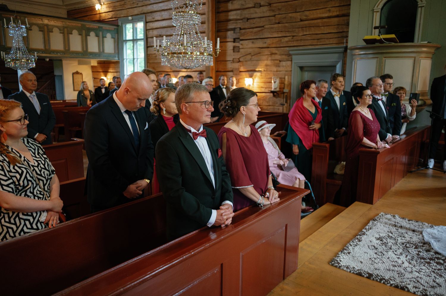 Wedding guests seated in wooden pews of a rustic log church.