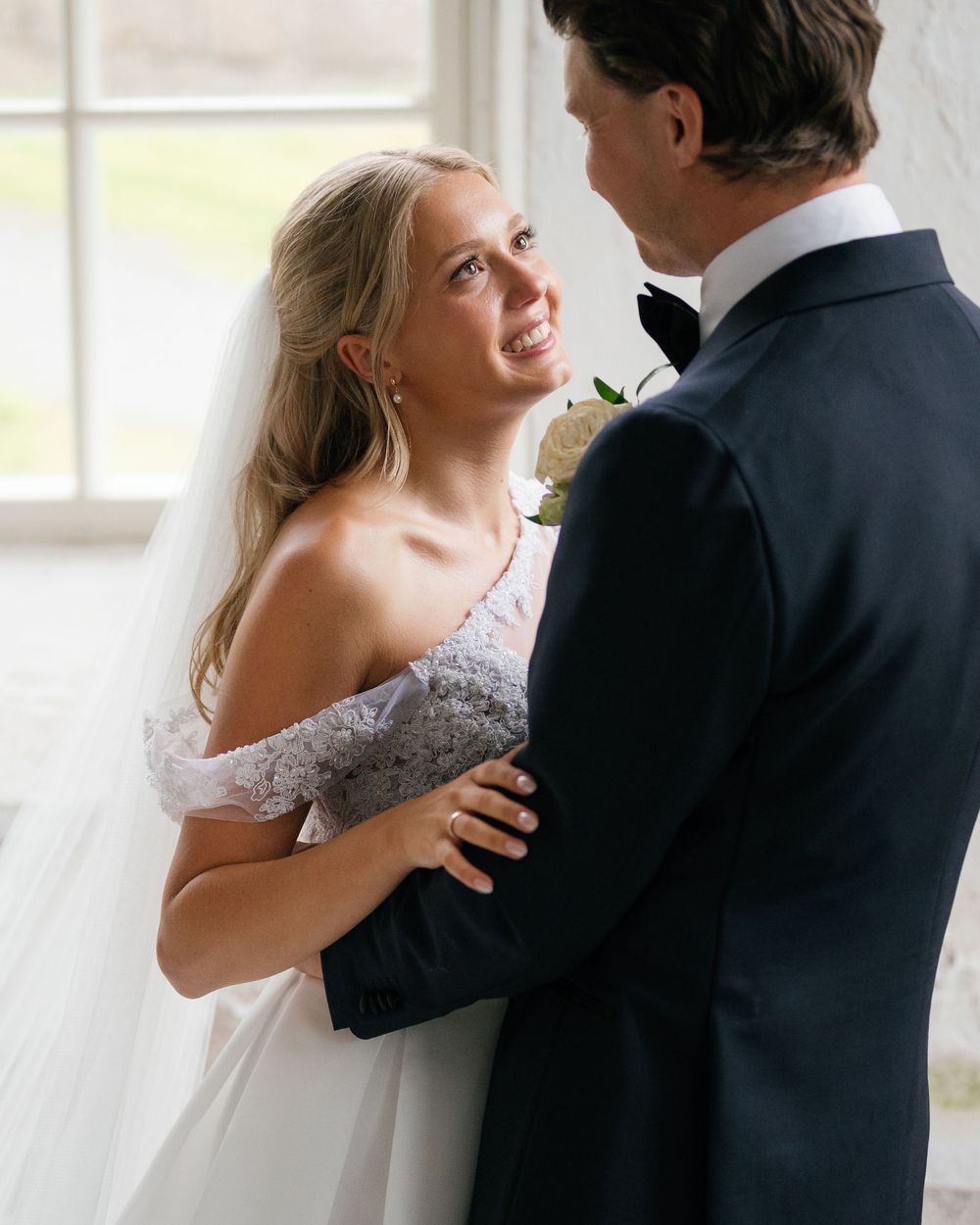 Romantic wedding couple embracing in sunlit room with vintage details.