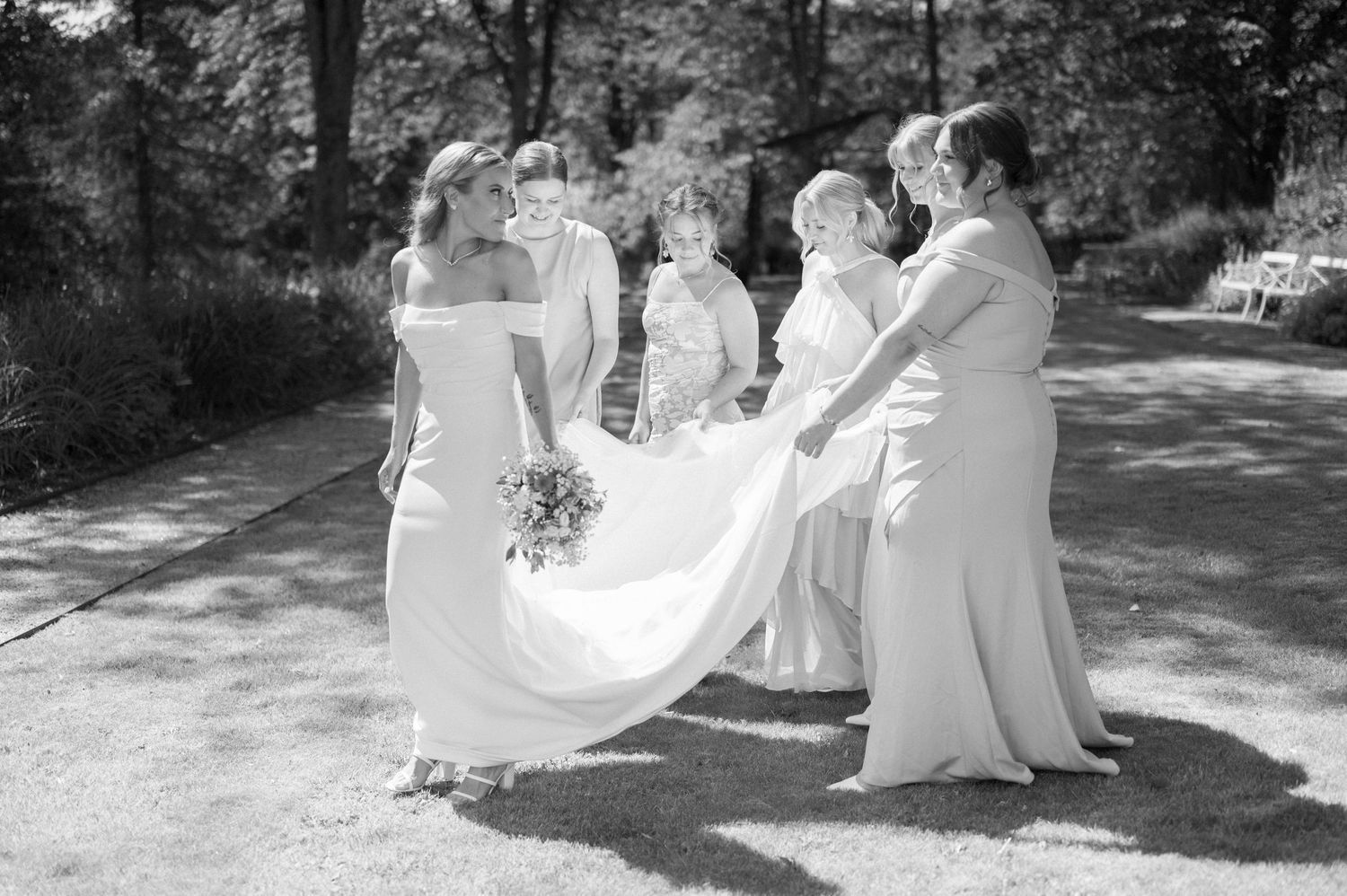 Black and white wedding photo of bridal party gathered outdoors in formal attire.