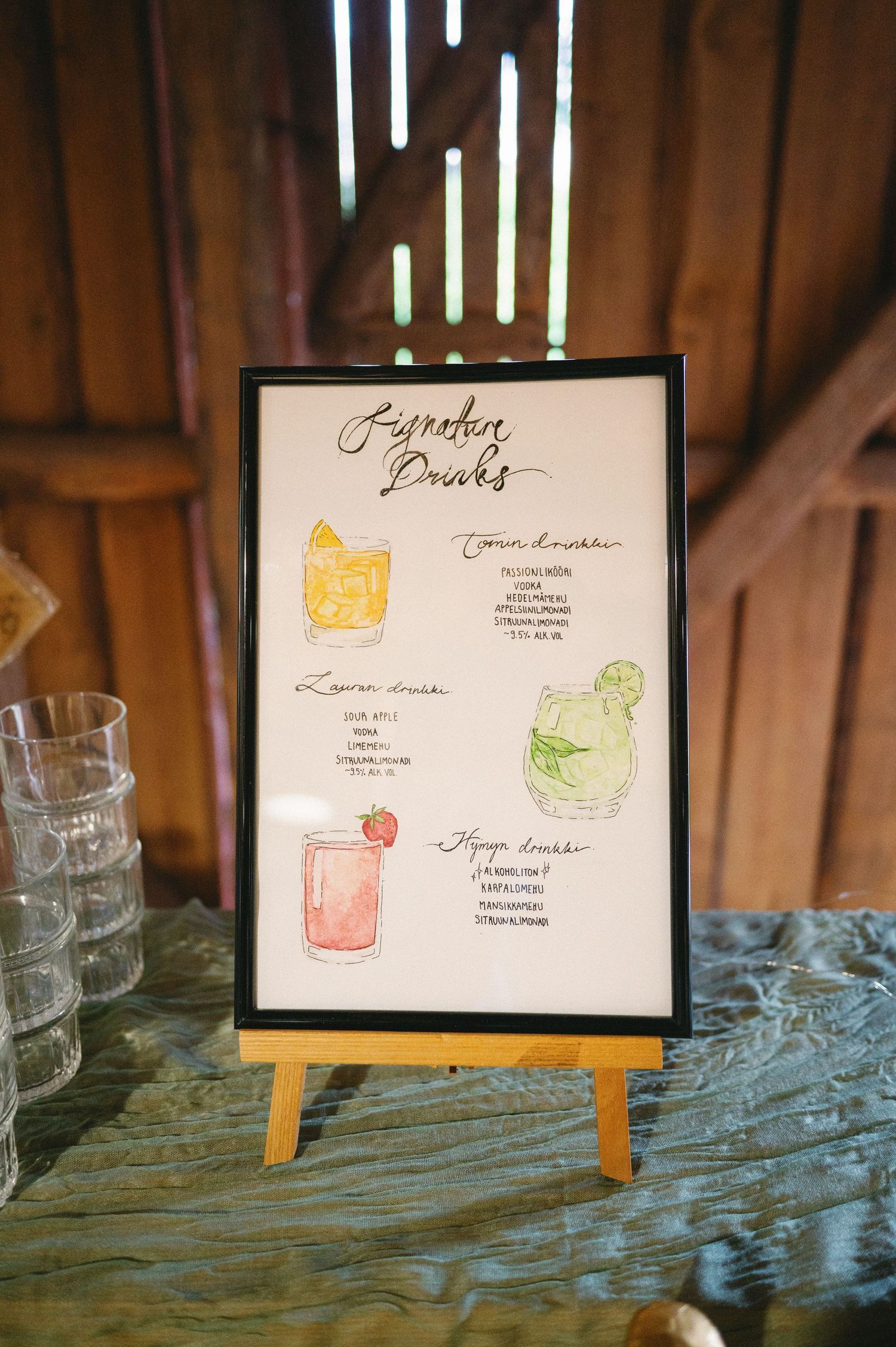 Framed cocktail menu displays with watercolor drink illustrations on rustic wooden surface.