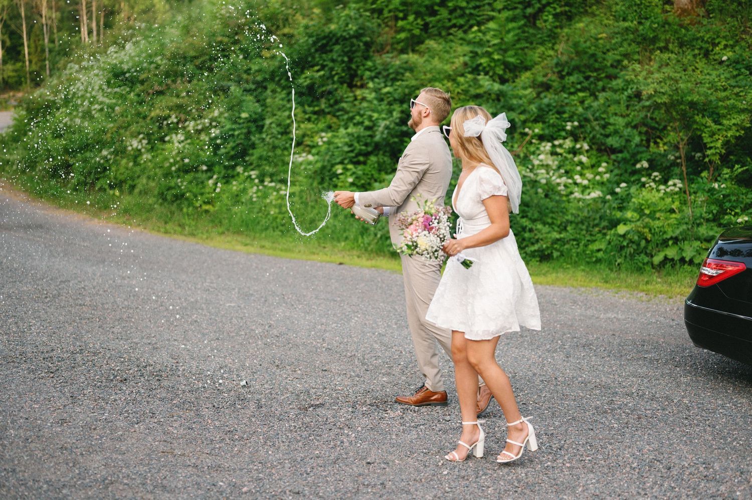 People walk along a gravel path carrying bouquets and balloons in a natural outdoor setting.
