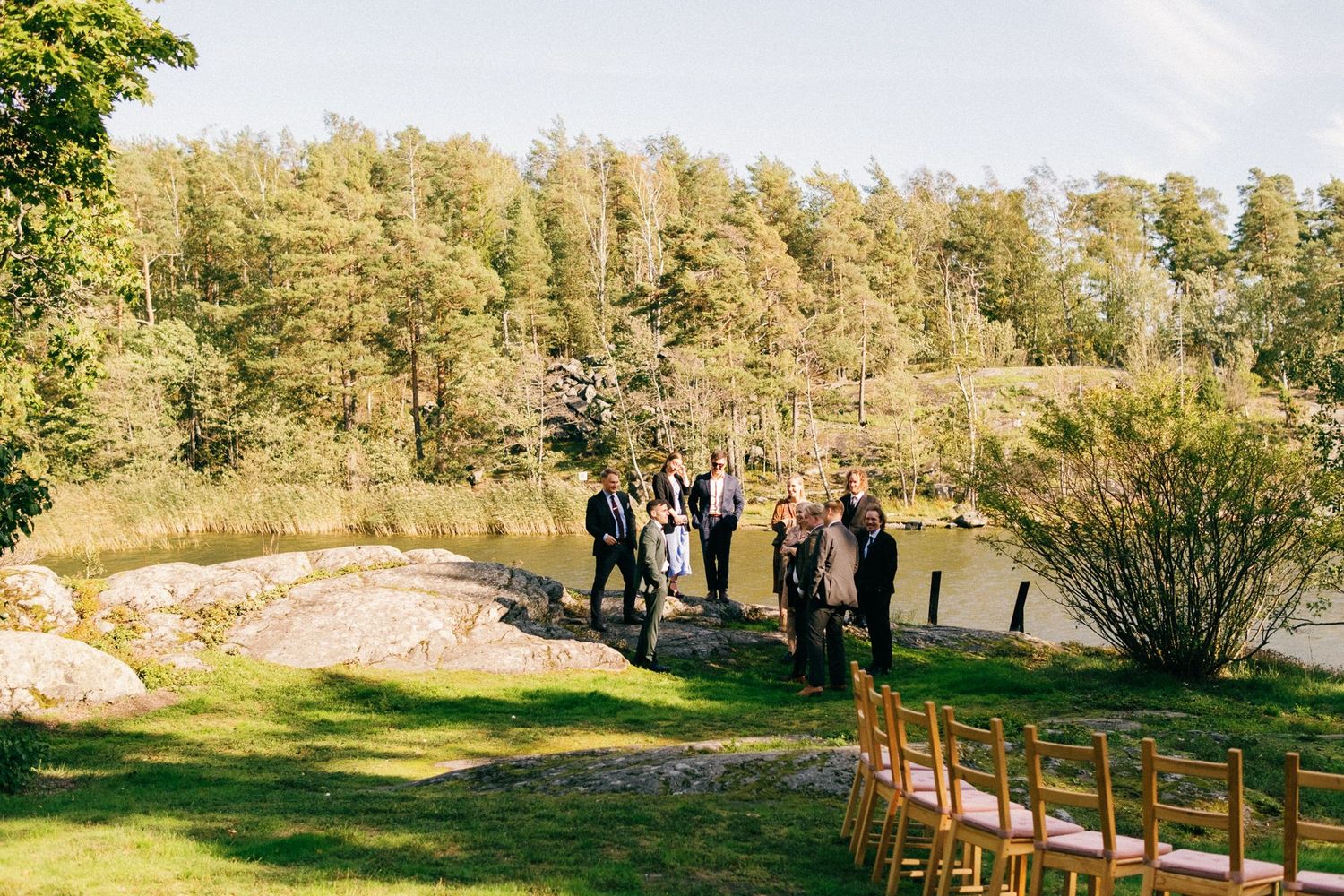 A wedding ceremony setup overlooking a lake with chairs and guests gathered in natural surroundings.