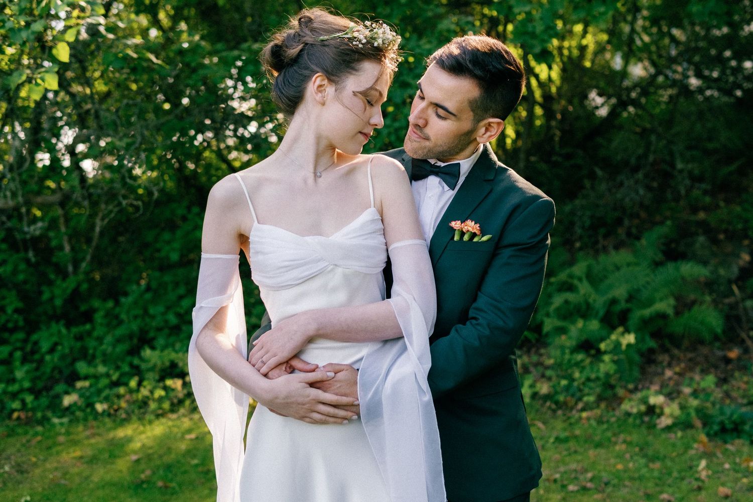 Romantic wedding couple embracing in a sunlit garden with green foliage.