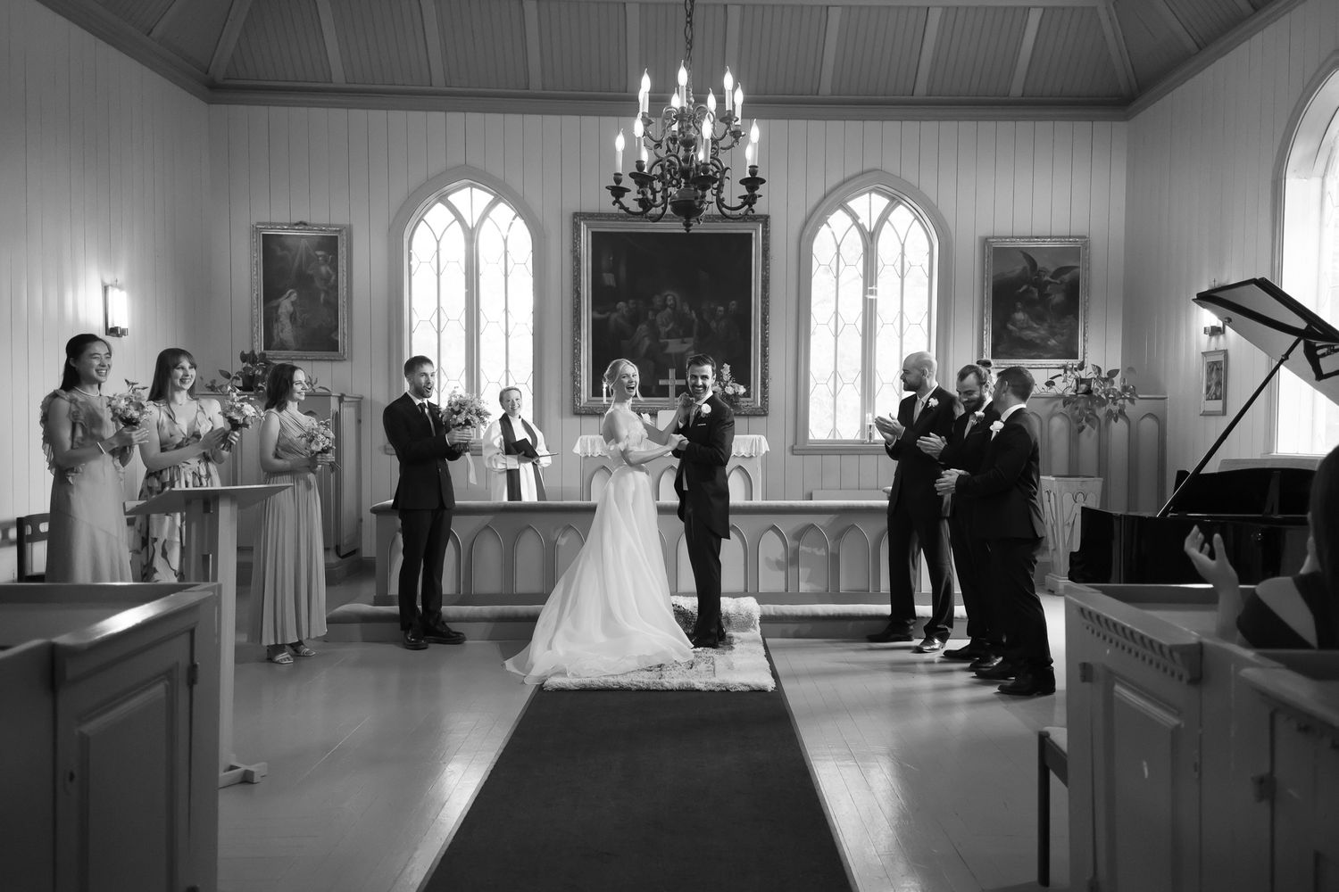 Black and white wedding ceremony photo inside a charming church with bride, groom, and wedding party at the altar.