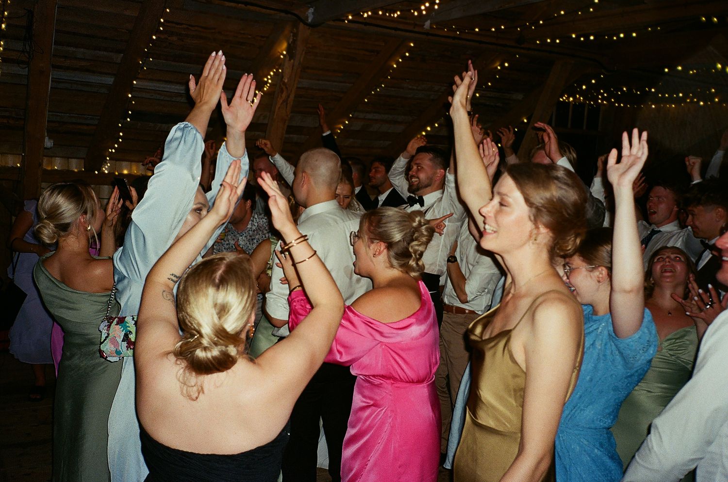 People dancing with raised hands in a dimly lit room with twinkling lights in the background.