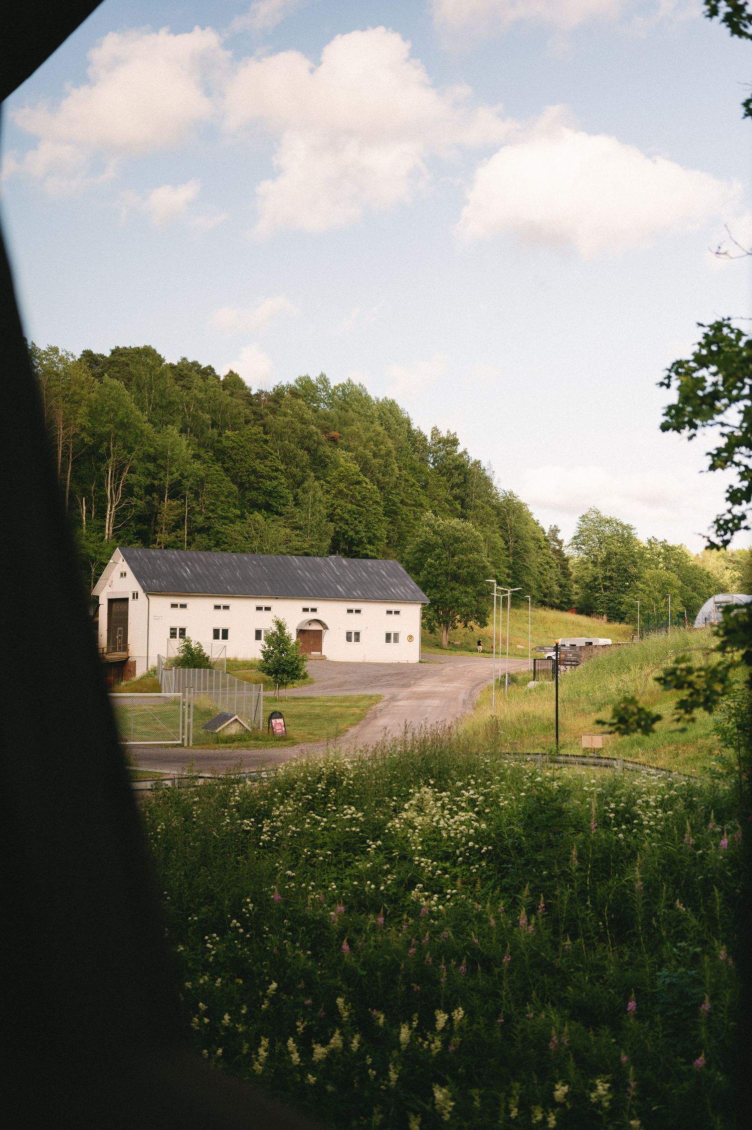 A white building nestled among trees on a hillside with a winding driveway on a sunny day.