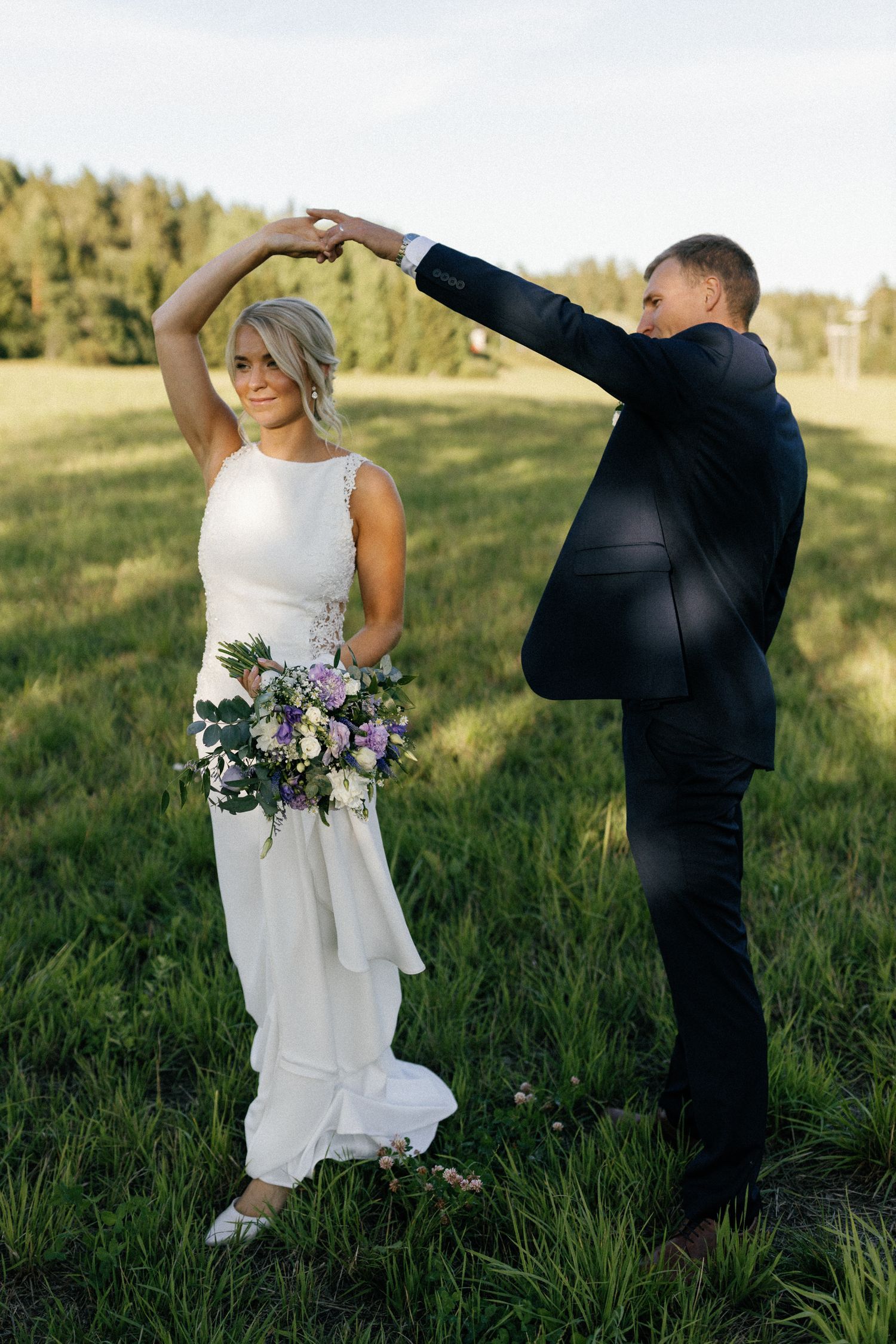 Playful moment of couple dancing in field with bride holding floral bouquet.