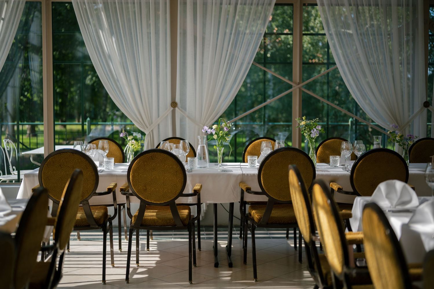 Elegant dining room with white tablecloths and gold chairs set for a formal event.