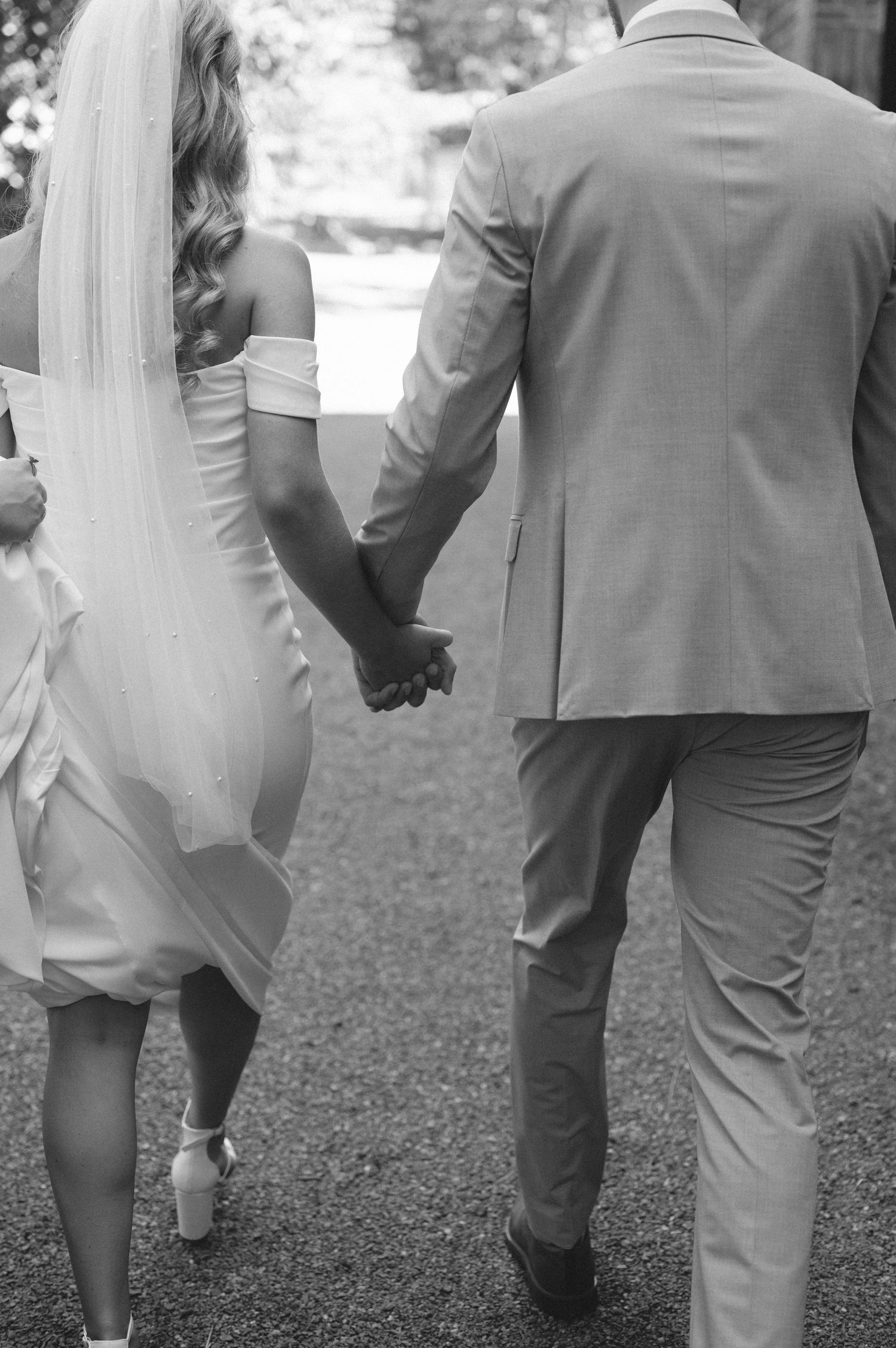 Wedding couple walks hand in hand on gravel path in black and white.