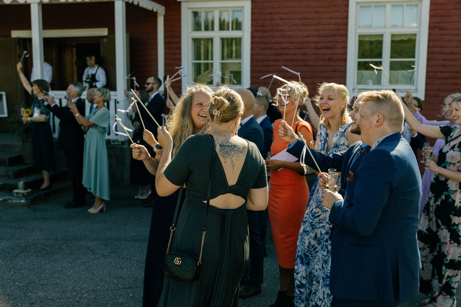 Wedding guests take photos outside traditional red building.