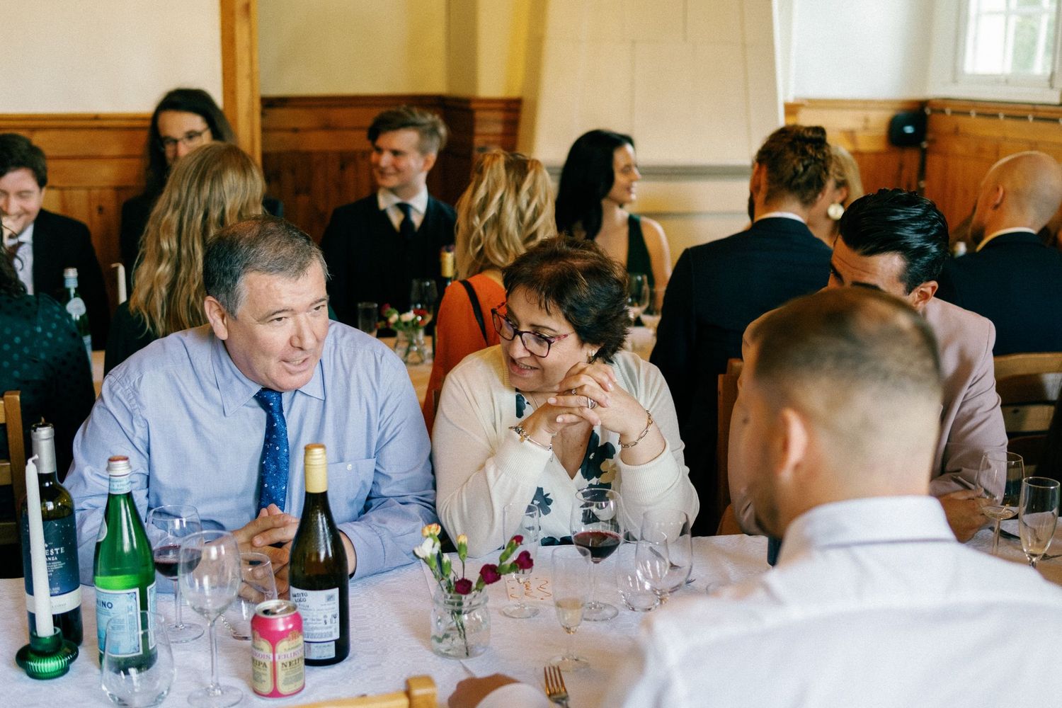 Guests seated at long tables with wine glasses and bottles during an indoor reception.
