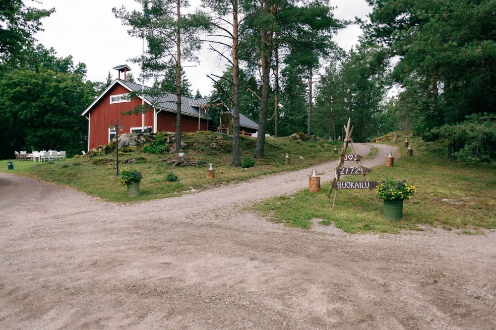 Dirt road winding through a wooded area with red buildings visible in the distance.