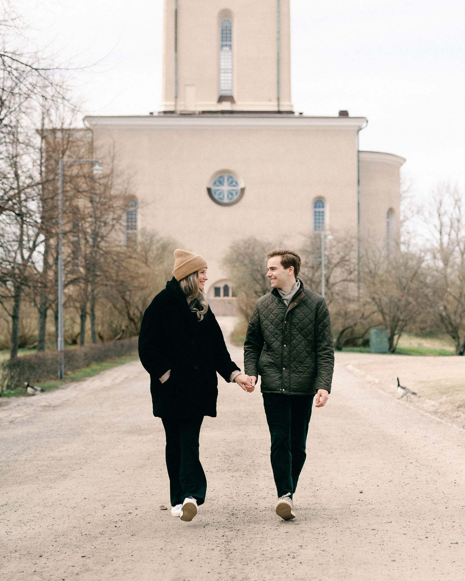 Two people walking together on a path in front of a church building with a tall tower.