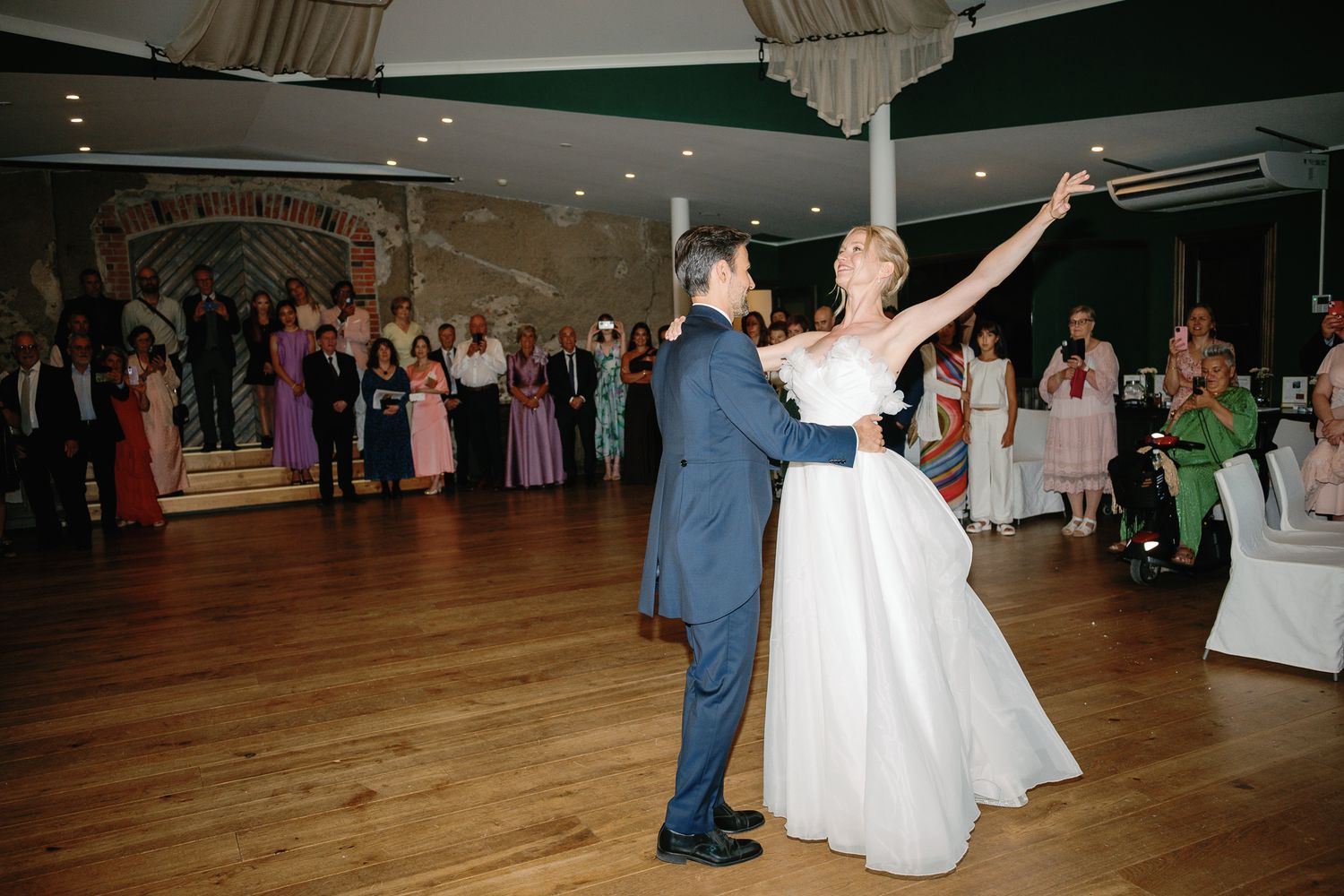 Bride and groom share their first dance at wedding reception while guests watch in elegant venue.