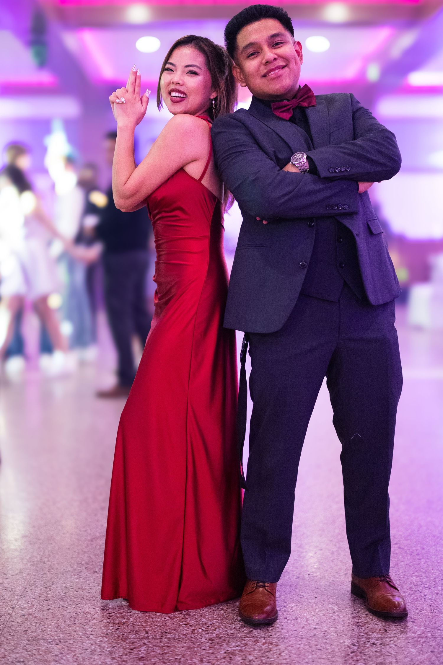 Couple poses back to back at quinceañera reception, woman in red gown and man in dark suit.