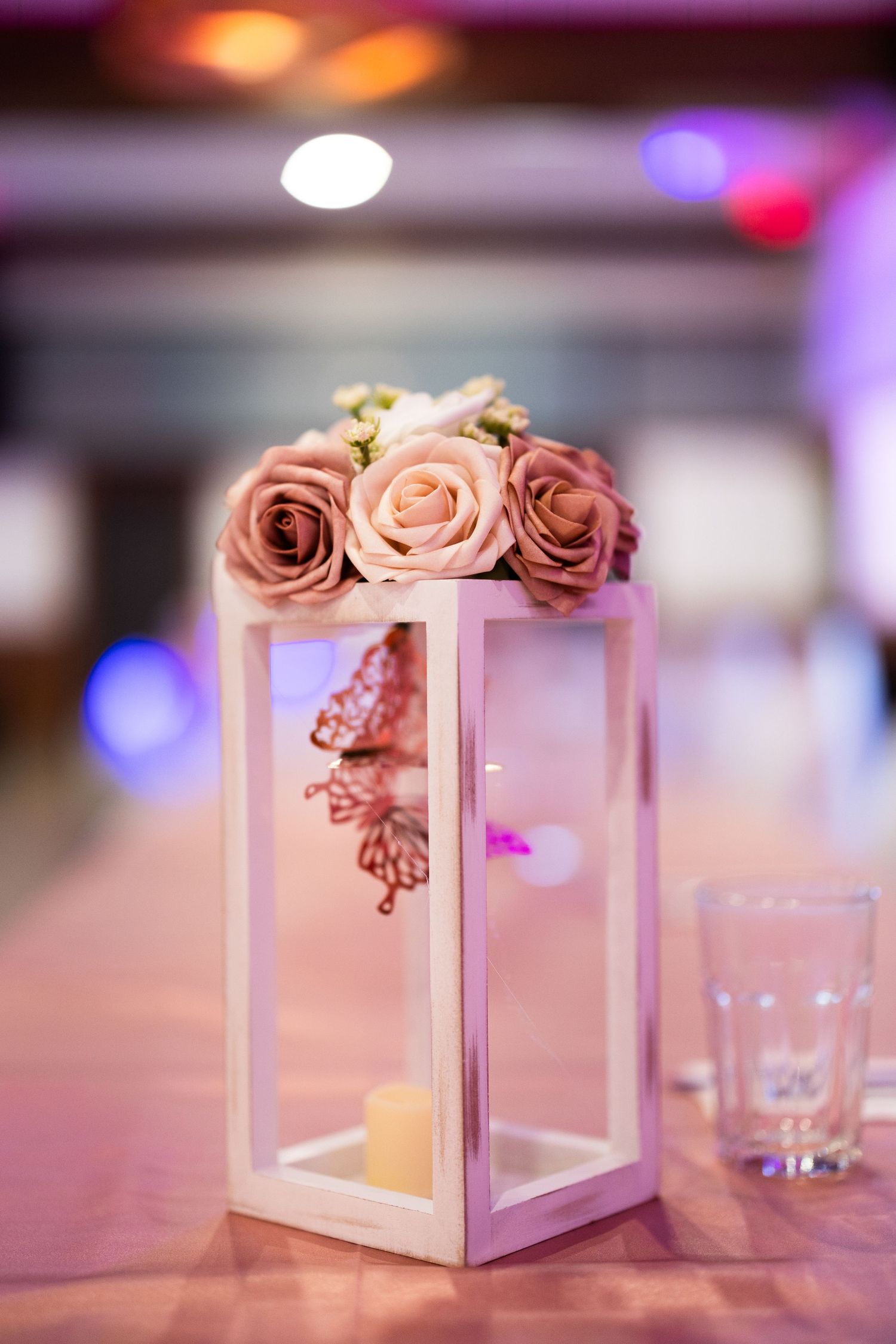 Elegant white lantern centerpiece with pink roses and butterfly decorations on a banquet table.
