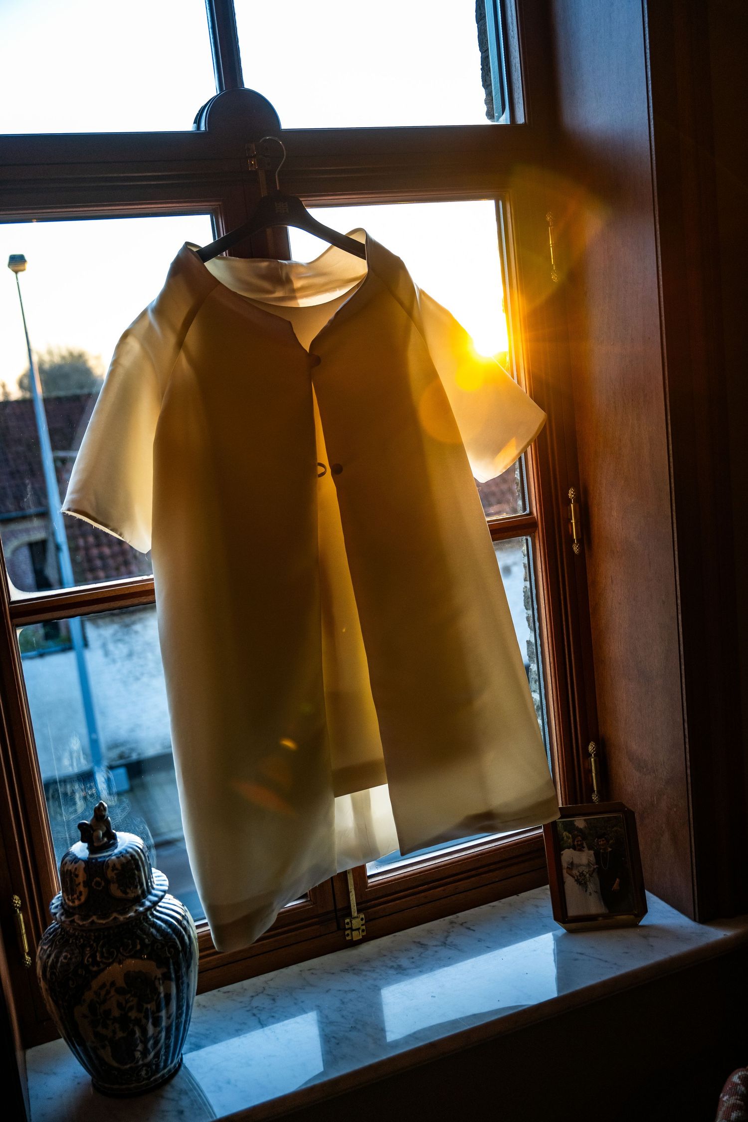 Trouwkleed gefotografeerd bij ruit met weerspiegeling van zonlicht