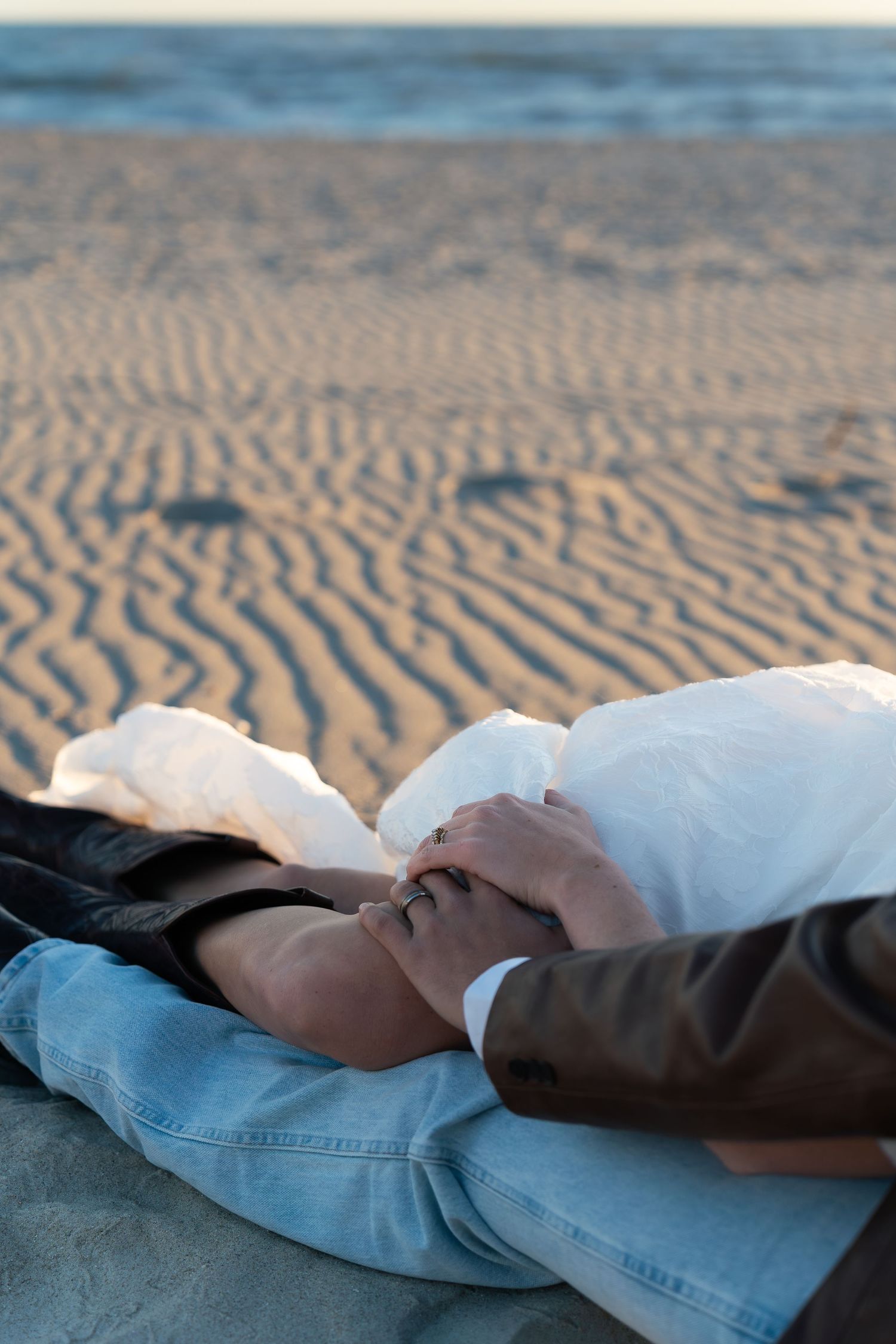 Couple holding hands while lying on sandy beach at sunset, romantic seaside moment.