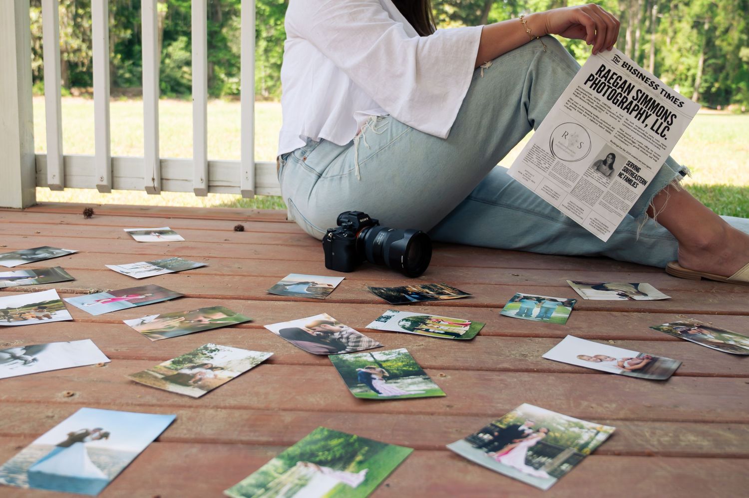 Photographer sitting on wooden deck reviewing printed photos scattered around with a camera and nature photography brochure.