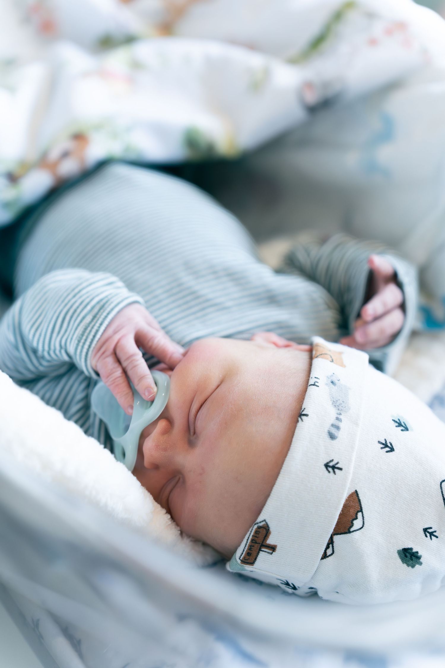 Sleeping baby wearing a white patterned onesie lies peacefully in a crib with soft blue bedding.