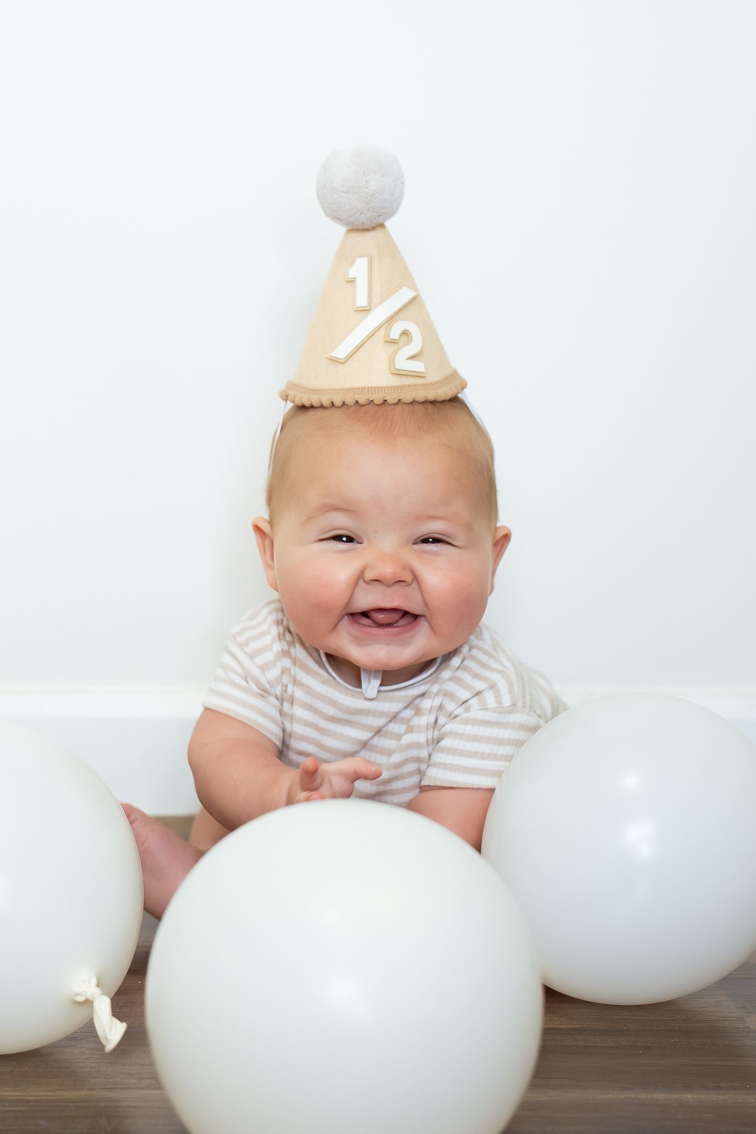 Smiling baby in party hat with white balloons against white background.