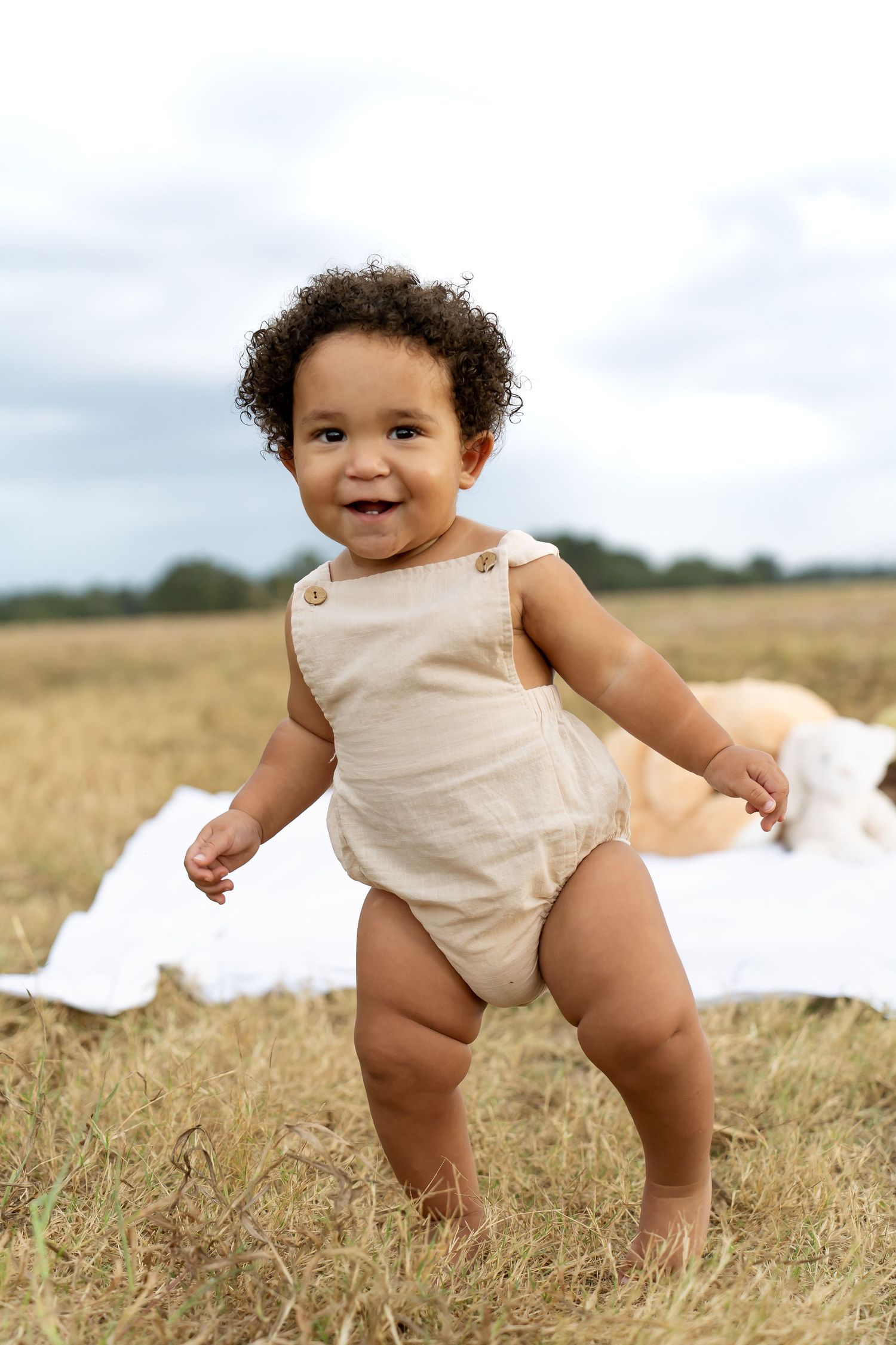 Baby in cream-colored outfit crawls and plays in a sunny wheat field.