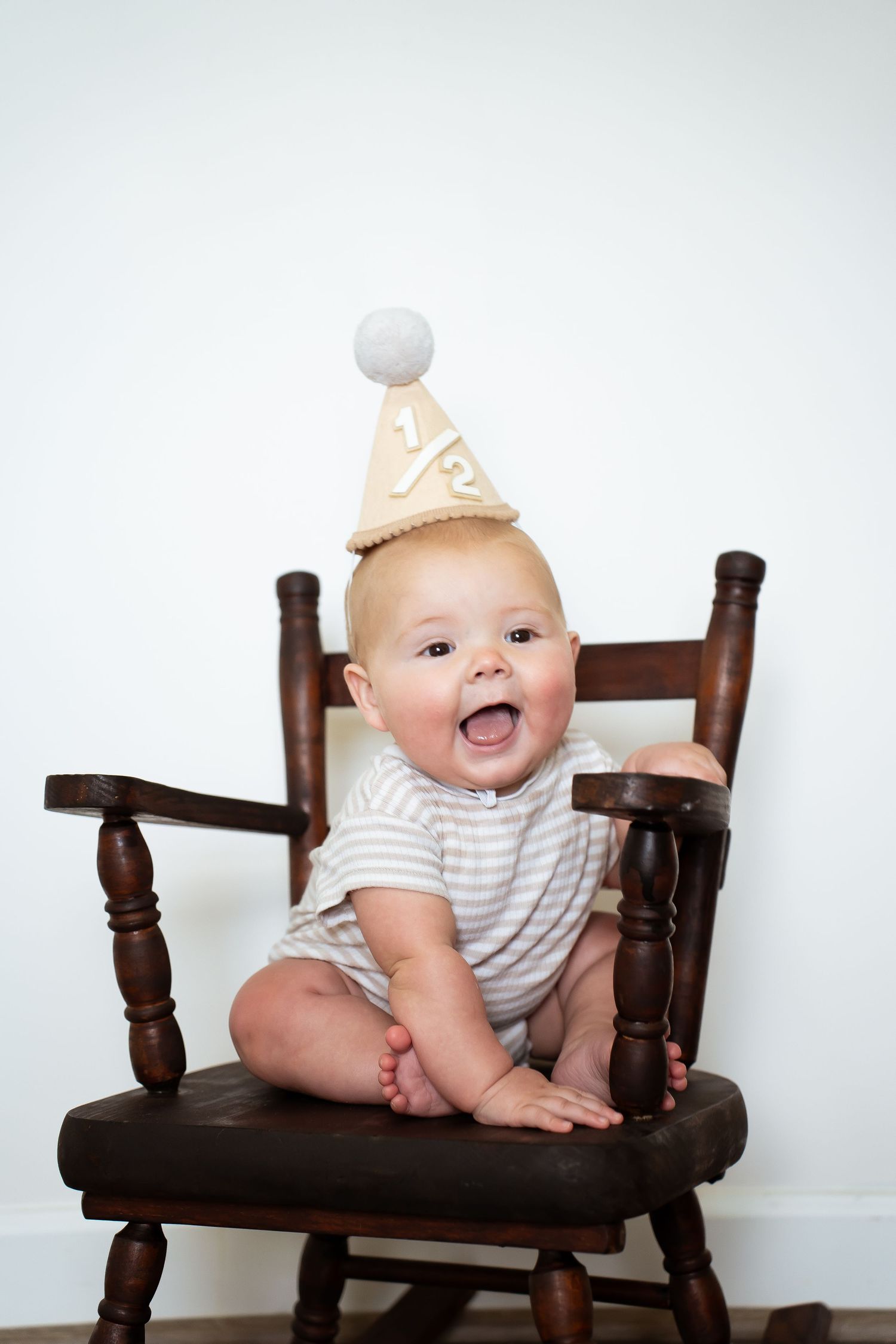 Joyful baby posing on wooden bench with festive party hat.