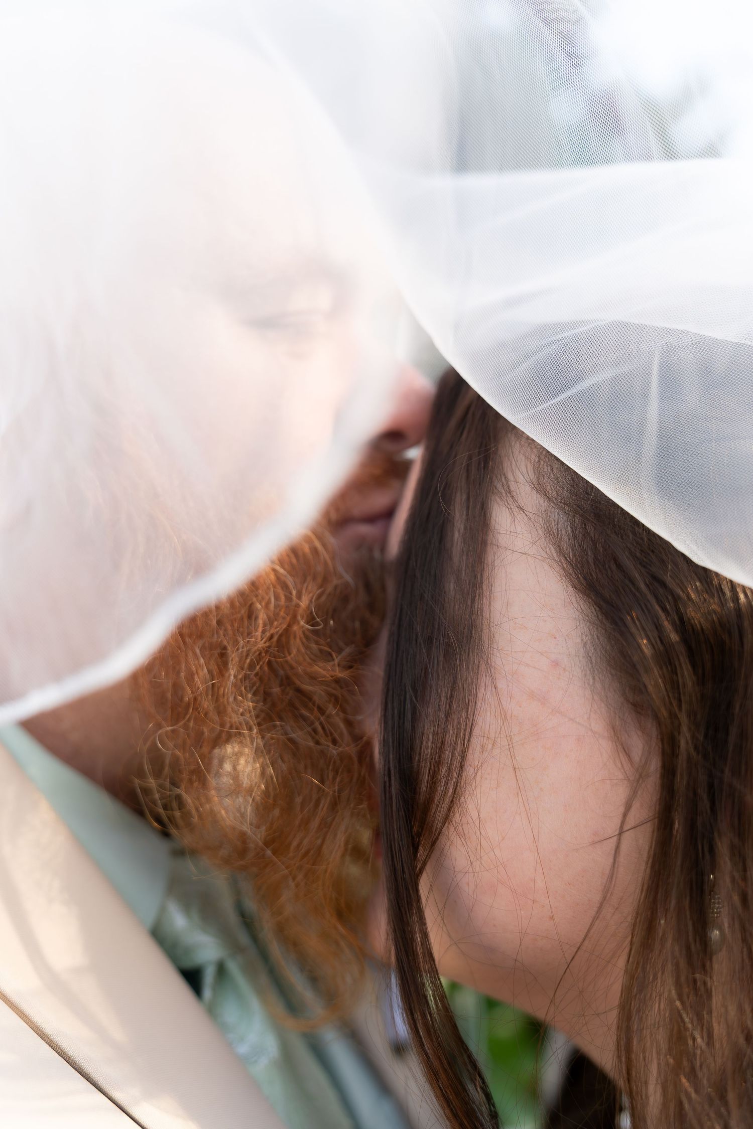 A close-up view of a person partially obscured by a white veil, revealing brown hair and part of their face.