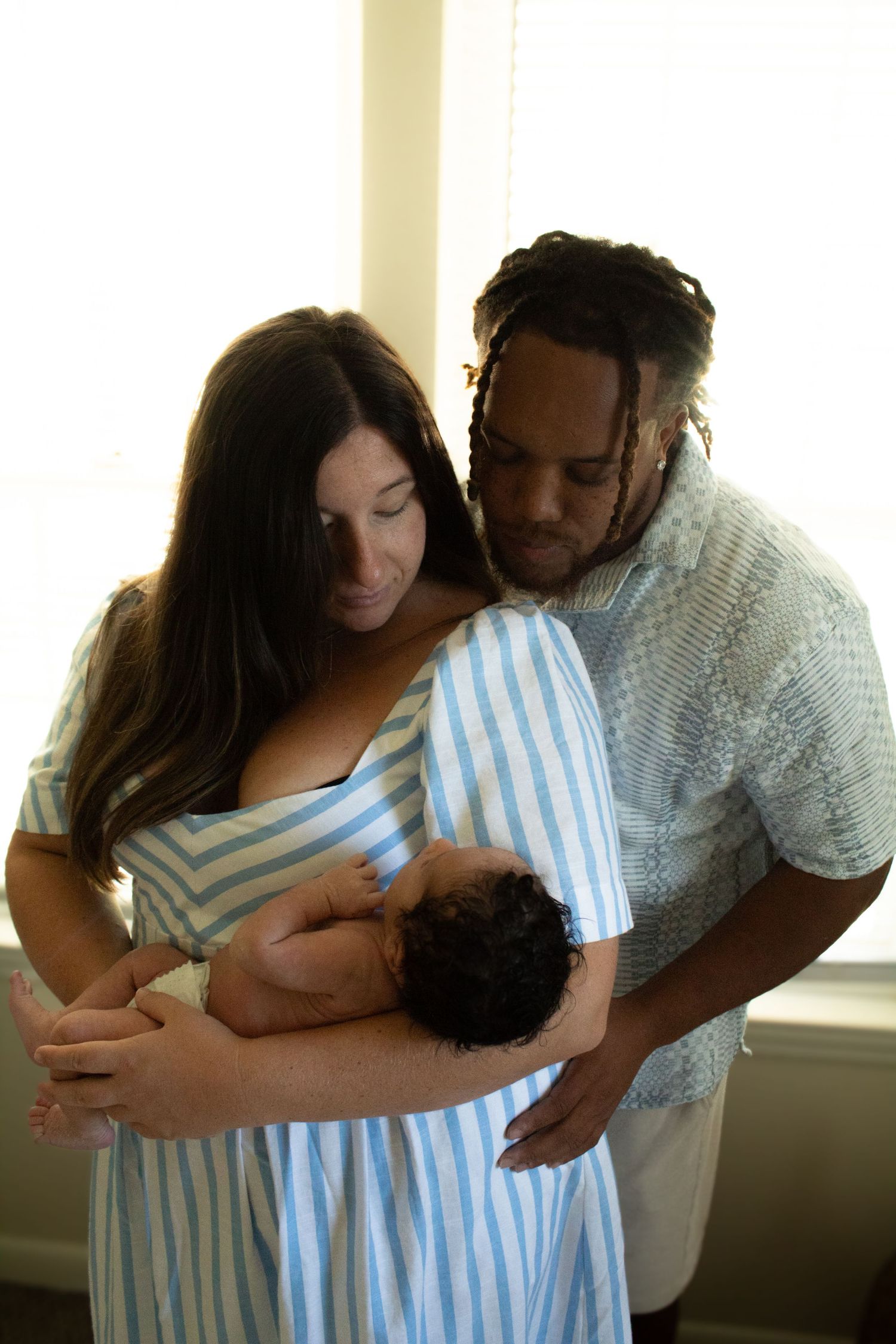 Parents sharing tender moment with newborn baby in sunlit room.