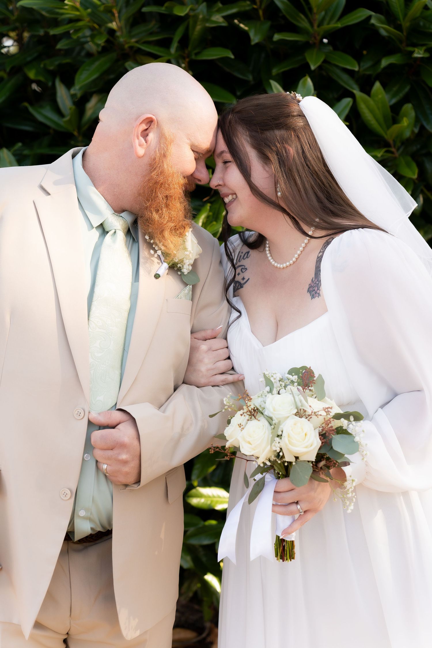 Bride and groom in white and beige sharing intimate moment with floral bouquet.
