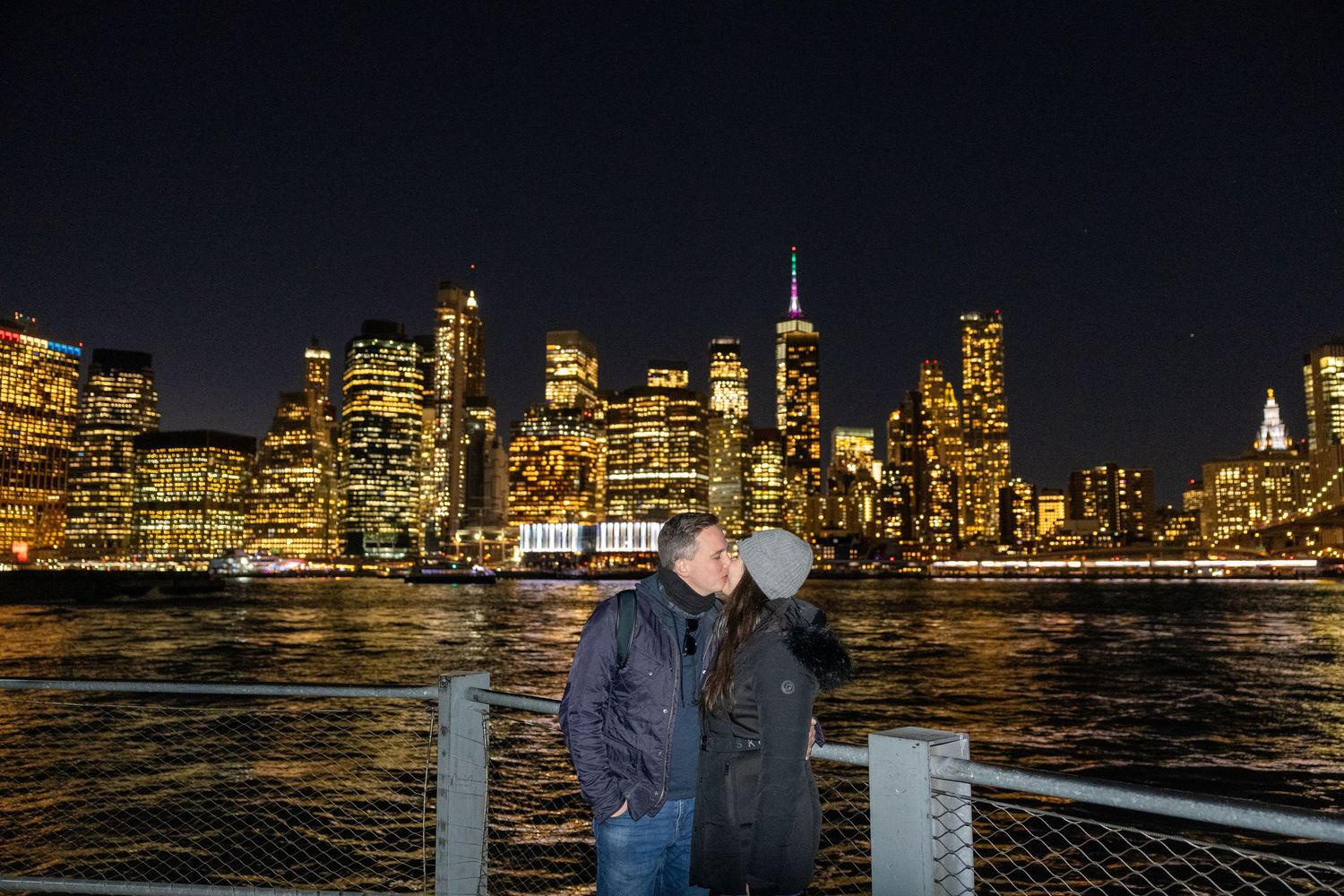 Romantic couple embracing with illuminated Manhattan skyline and bridge at night.