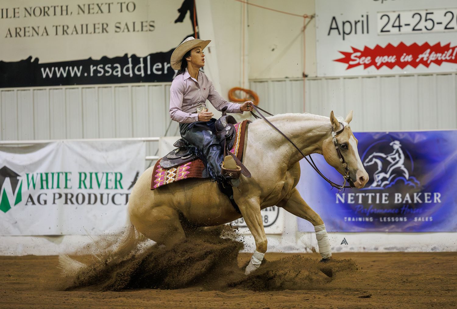 Rider on palomino horse performing reining maneuver in indoor arena during Nettie Baker training competition.